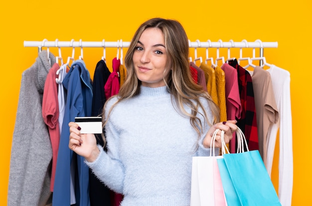 Jovem mulher em uma loja de roupas, segurando um cartão de crédito e com sacolas de compras