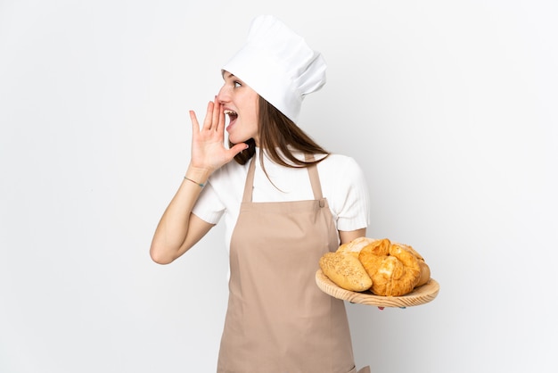 Jovem mulher em uniforme de chef isolado no branco gritando com a boca aberta