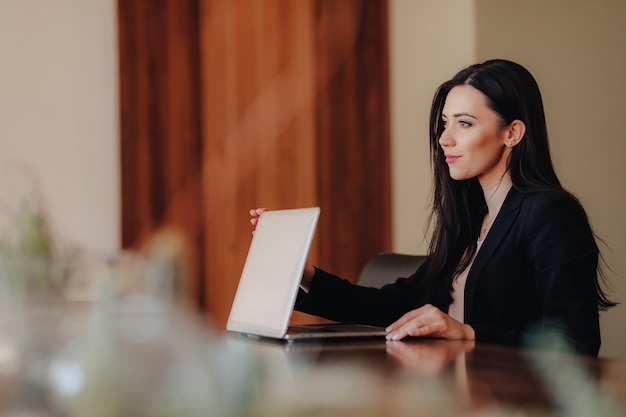 Jovem mulher emocional atraente em roupas de estilo empresarial, sentado a mesa com um laptop