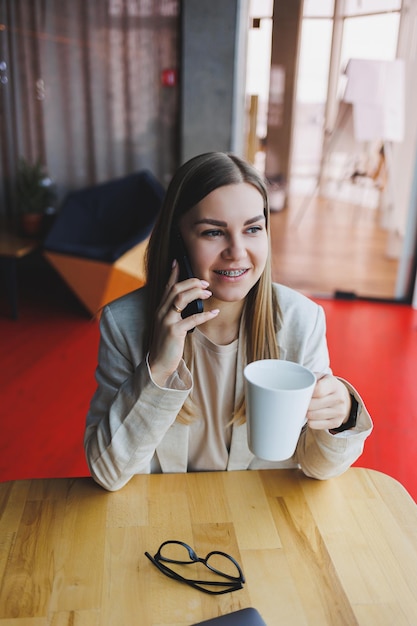 Foto jovem mulher encantadora ligando com um telefone celular enquanto está sentado sozinho em um café em seu tempo livre mulher atraente com um sorriso doce falando com um telefone celular enquanto relaxa em um café