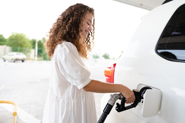 Jovem mulher encaracolada reabastecendo carro no posto de gasolina