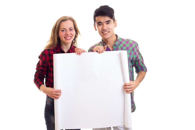 Jovem mulher engraçada com jovem bonito com cabelo escuro em camisas xadrez segurando cartaz branco