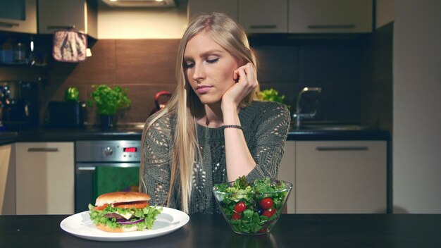 Foto jovem mulher escolhendo entre hambúrguer e salada