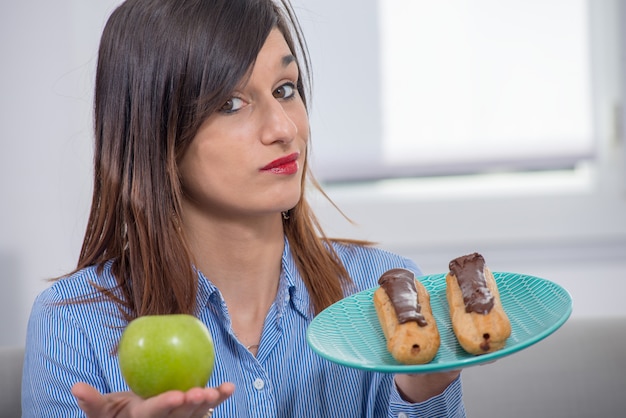 Jovem mulher escolhendo entre uma maçã e pastelaria de chocolate