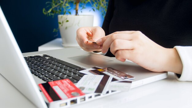 Jovem mulher escolhendo o cartão de crédito para fazer compras online no laptop de casa. conceito de compras online e e-commerce.