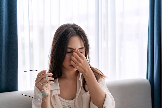 Jovem mulher esfregando os olhos sente dor e tira os óculos sentados no sofá e descansa os olhos em casa Problema de visão