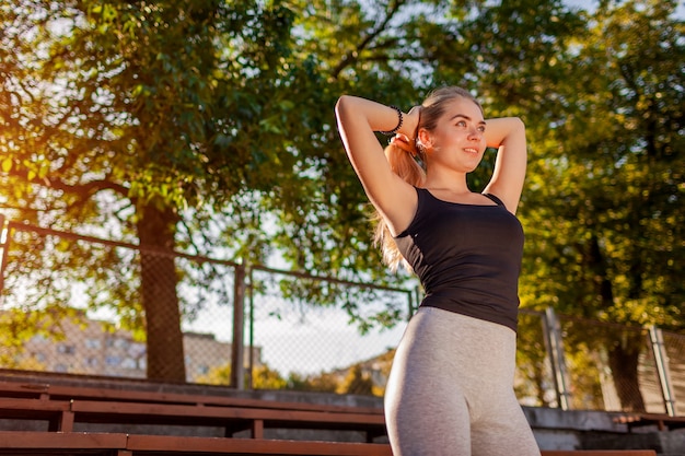 Jovem mulher esportiva, amarrando o cabelo em um rabo de cavalo no campo de esportes no verão. Preparação para treino ao ar livre