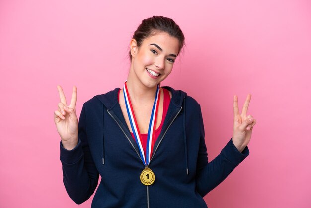 Jovem mulher esportiva brasileira com medalhas isoladas em fundo rosa, mostrando sinal de vitória com as duas mãos