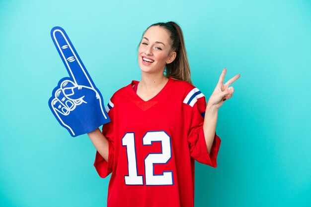 Jovem mulher esportiva caucasiana isolada em fundo azul sorrindo e mostrando sinal de vitória