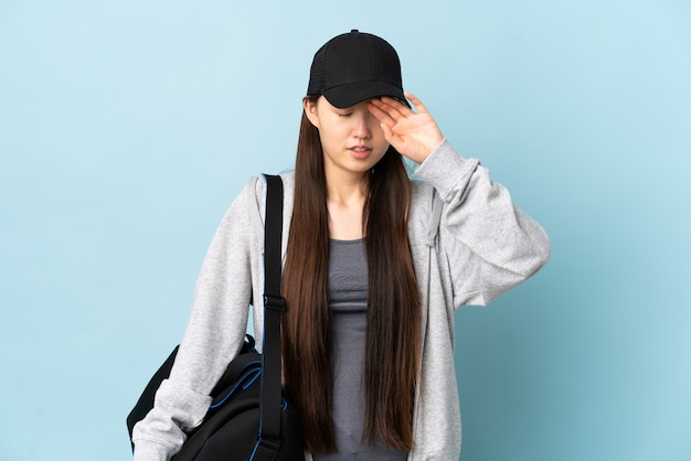 Jovem mulher esportiva chinesa com bolsa esportiva sobre fundo azul isolado com expressão cansada e doente