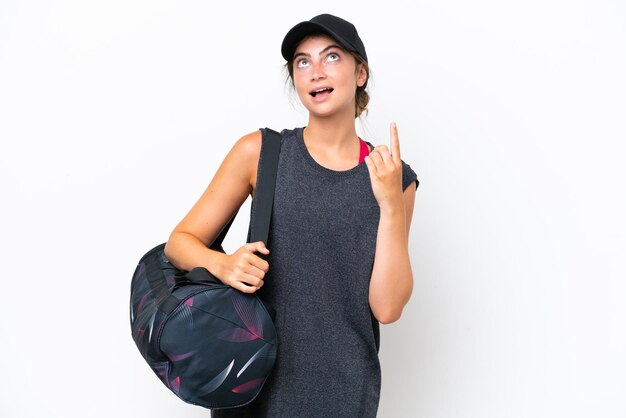 Jovem mulher esportiva com bolsa esportiva isolada em fundo branco apontando para cima e surpreendida