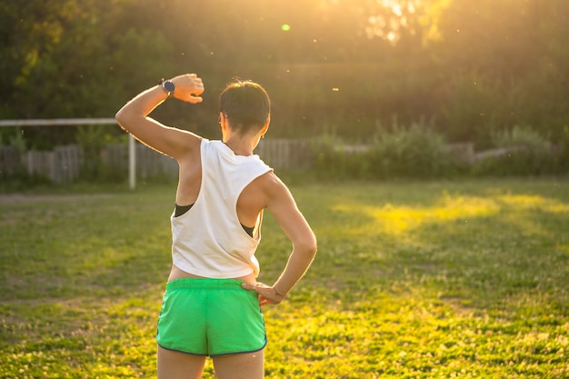 Jovem mulher esportiva com cabelo preto curto se alongando antes de correr em um parque, aquecer antes do treino ao ar livre