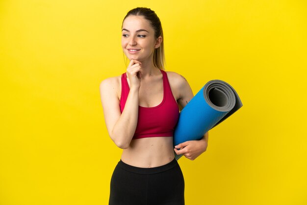 Jovem mulher esportiva indo para aulas de ioga, segurando uma esteira, olhando para o lado e sorrindo