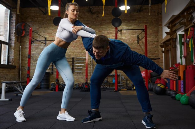 Jovem mulher esportiva praticando grappling em duelo com treinador pessoal