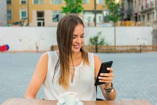 Jovem mulher está assistindo móvel enquanto ela está tomando café