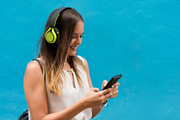 Jovem mulher está ouvindo música com seus fones de ouvido no fundo azul