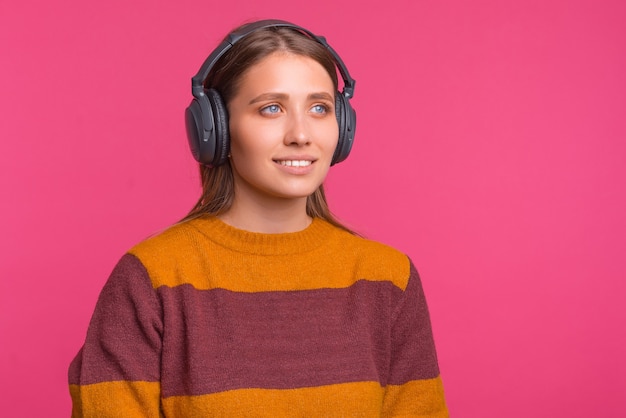 Jovem mulher está usando um par de fones de ouvido sobre fundo rosa.