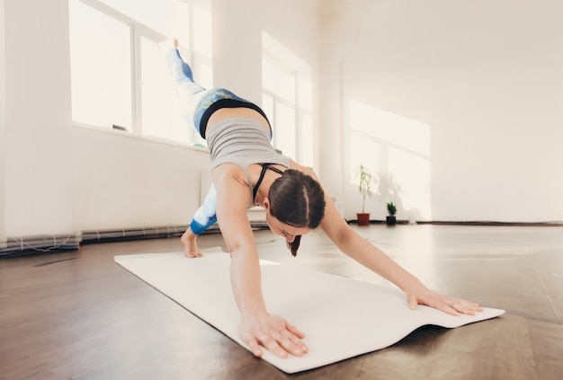 Jovem mulher esticando e fazendo exercícios de ioga no estúdio