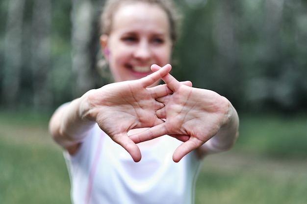 Jovem mulher esticando os braços ao ar livre. fitness feminino fazendo exercícios de aquecimento no parque, concentre-se nas mãos