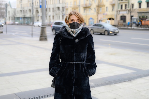 Jovem mulher europeia com máscara médica preta protetora descartável na cidade ao ar livre