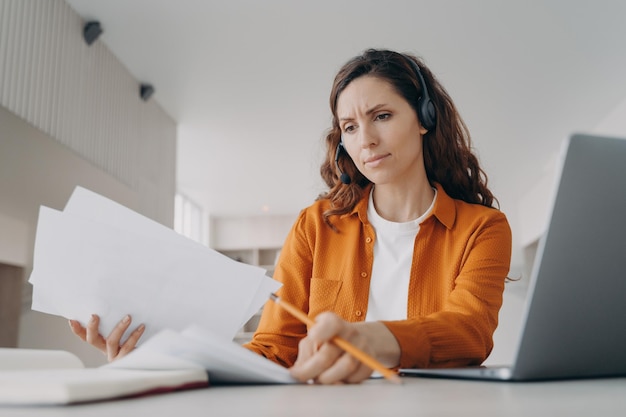 Jovem mulher europeia examina relatórios e gráficos o gerente está fazendo brainstorming on-line em casa