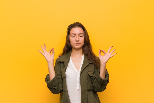 Jovem mulher europeia isolada sobre fundo amarelo relaxa após um árduo dia de trabalho, ela está realizando ioga.