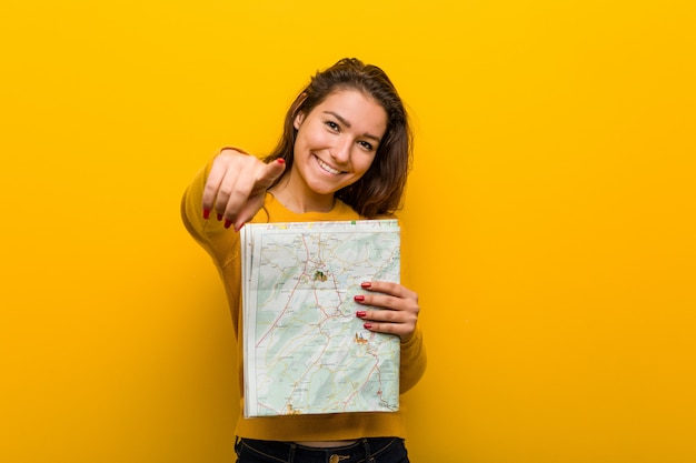 Jovem mulher Europeia segurando um sorriso alegre de mapa apontando para a frente.