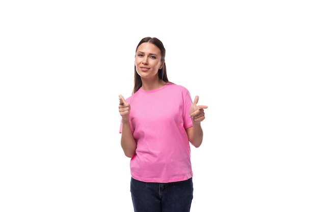 Jovem mulher europeia sorridente com cabelo preto em uma camiseta rosa aponta para uma ideia com o dedo em um