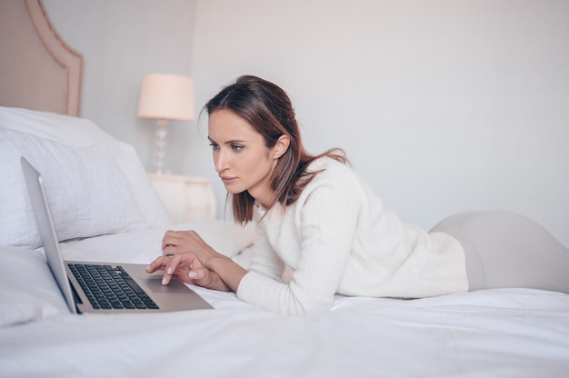 Jovem mulher europeia trabalhando em um laptop no quarto branco