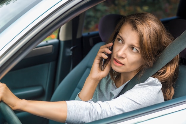 Jovem mulher falando ao telefone enquanto está sentado no carro.