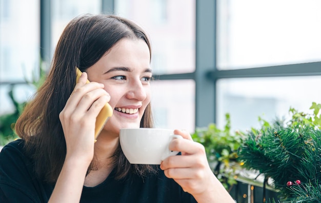 Jovem mulher falando ao telefone enquanto está sentado perto da janela em um café