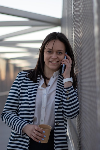 Jovem mulher falando ao telefone inclinada sobre malha de aço na ponte pedonal