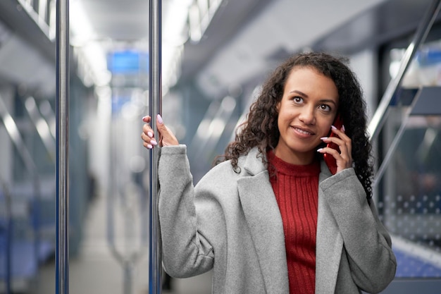 Jovem mulher falando em seu smartphone enquanto está em um vagão de metrô