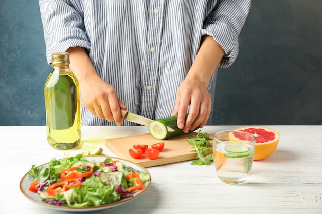 Jovem mulher fatias de pepino para salada na madeira