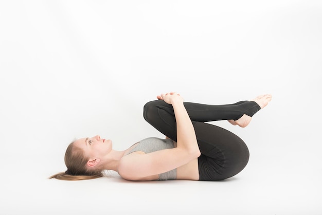 Jovem mulher faz ioga com os joelhos contra o peito em fundo branco. Técnica de execução de asanas. meditação.