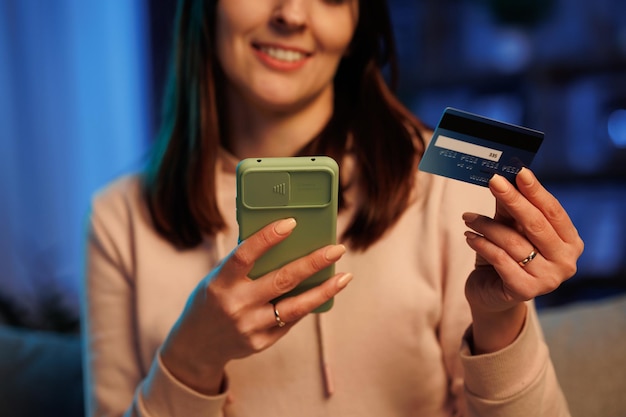 Jovem mulher fazendo compras on-line segurando o cartão de crédito sentado em casa Compradora feliz fazendo compras na loja on-line Pagamentos fáceis instantâneos usando telefone inteligente Serviço de aplicativo bancário on-line