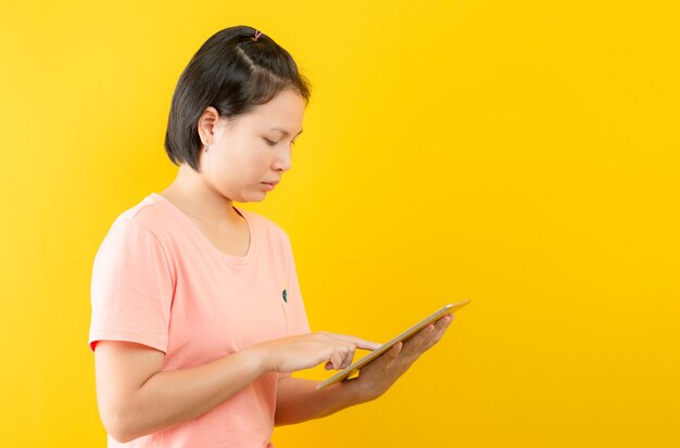 Jovem mulher fazendo compras online com ipad feliz em casa contra um fundo amarelo