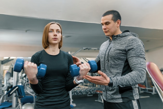 Jovem mulher fazendo exercícios com instrutor pessoal no ginásio.