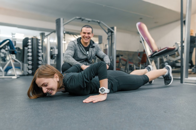 Jovem mulher fazendo exercícios com instrutor pessoal no ginásio