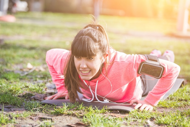 Jovem mulher fazendo exercícios de flexões no parque.