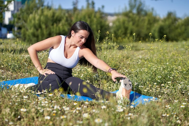 Jovem mulher fazendo exercícios de ginástica na grama. Modelo feminina em roupas esportivas