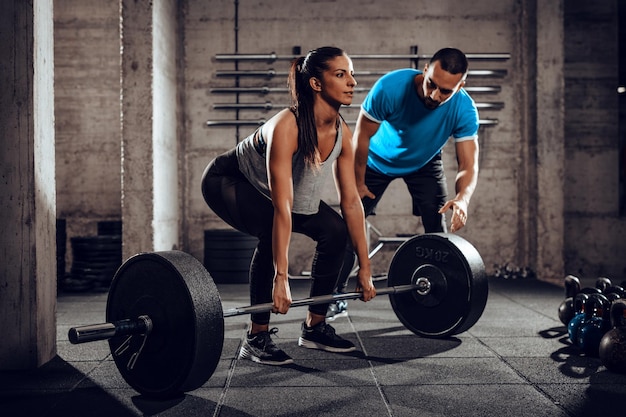 Jovem mulher fazendo exercícios duros na academia com um personal trainer.