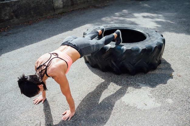 Jovem mulher fazendo flexões treinamento ao ar livre usando pneu gigante