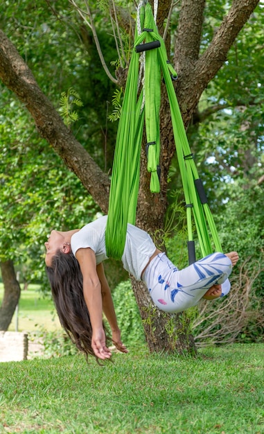 Jovem mulher fazendo ioga antigravidade em um parque em um dia ensolaradoImagem vertical