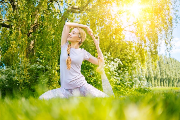 Jovem mulher fazendo ioga asana no parque, garota, exercícios de alongamento em posição de ioga, mulher feliz e saudável sentada em posição de lótus praticando ioga e meditação e esportes no pôr do sol ao ar livre