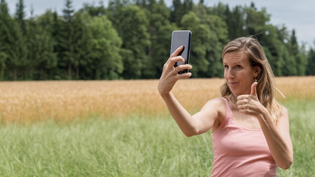 Jovem mulher fazendo selfies com seu celular na natureza mostrando um gesto de polegar para cima