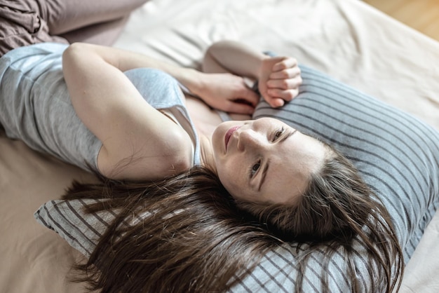 Jovem mulher feliz acordou de manhã e está deitada na cama com prazer Conceito de conforto de sono saudável e um começo agradável para um novo dia