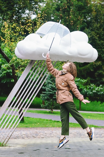 Jovem mulher feliz andando na chuva no parque verde com guarda-chuva, sorrindo. pessoa sentada no banco