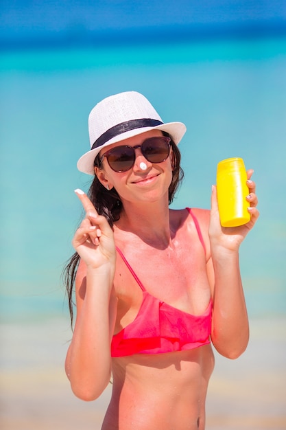 Jovem mulher feliz aplicando loção bronzeadora no nariz na praia branca