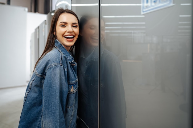 Foto jovem mulher feliz apoiada em sua nova geladeira em um shopping